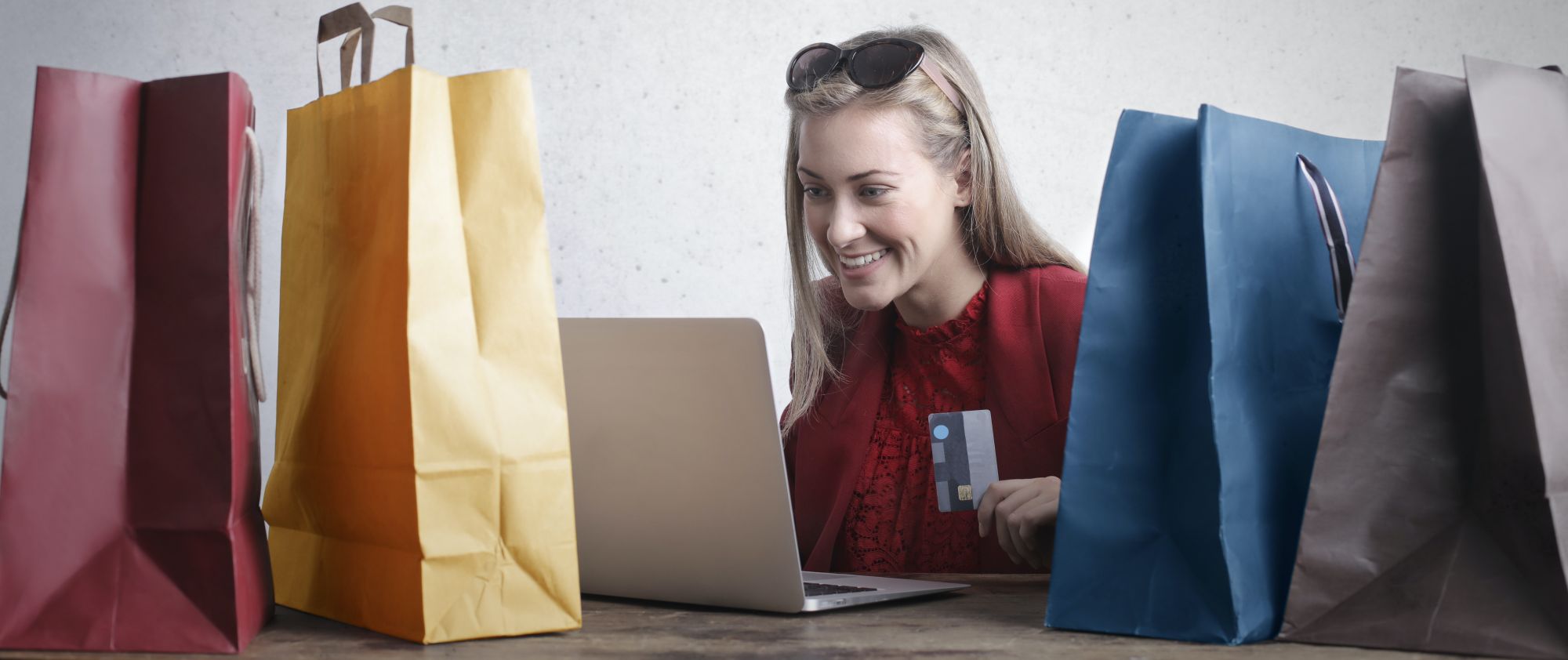 Woman holding credit card using laptop surrounded by colourful shopping bags